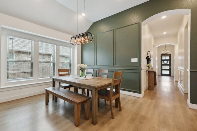 dining space featuring arched walkways, a chandelier, a decorative wall, light wood-style flooring, and vaulted ceiling