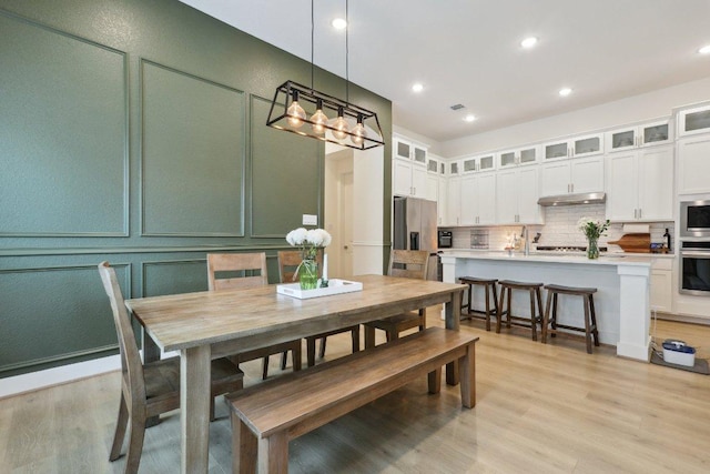 dining area featuring light wood-style floors, a chandelier, recessed lighting, and a decorative wall