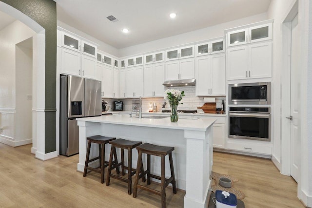 kitchen with stainless steel appliances, under cabinet range hood, light countertops, decorative backsplash, and light wood-style flooring