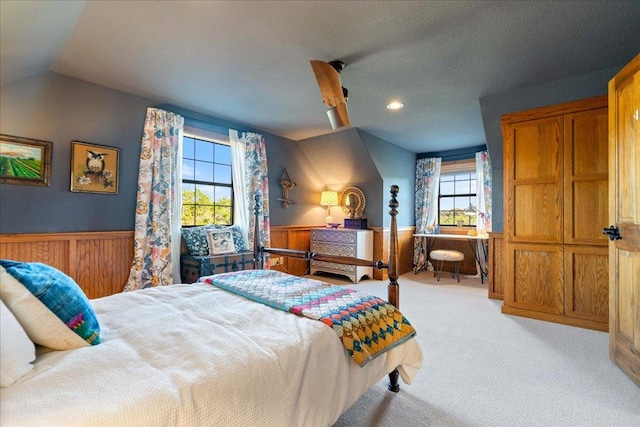 carpeted bedroom with wood walls, wainscoting, ceiling fan, and vaulted ceiling
