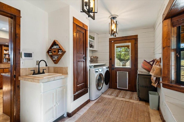 laundry area with a sink, cabinet space, wood walls, and independent washer and dryer
