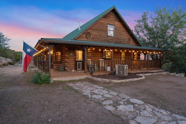 back of property at dusk featuring metal roof, central AC, covered porch, and log siding