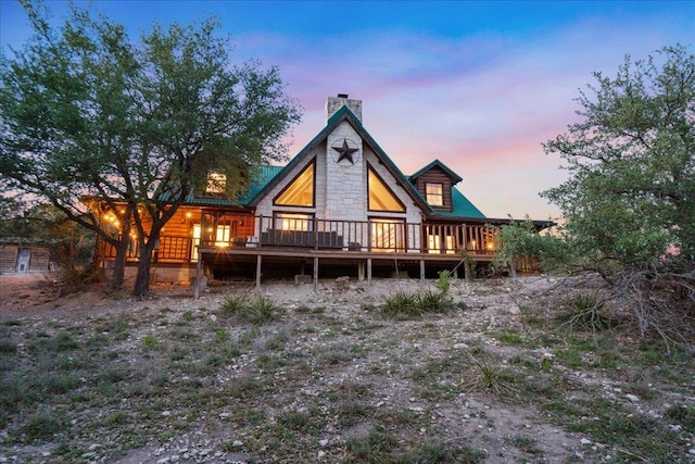 rear view of property featuring a wooden deck, stone siding, and a chimney