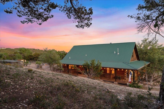 back of house at dusk featuring covered porch and metal roof