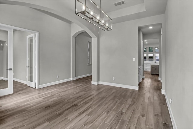unfurnished dining area featuring french doors, visible vents, arched walkways, baseboards, and dark wood-style floors