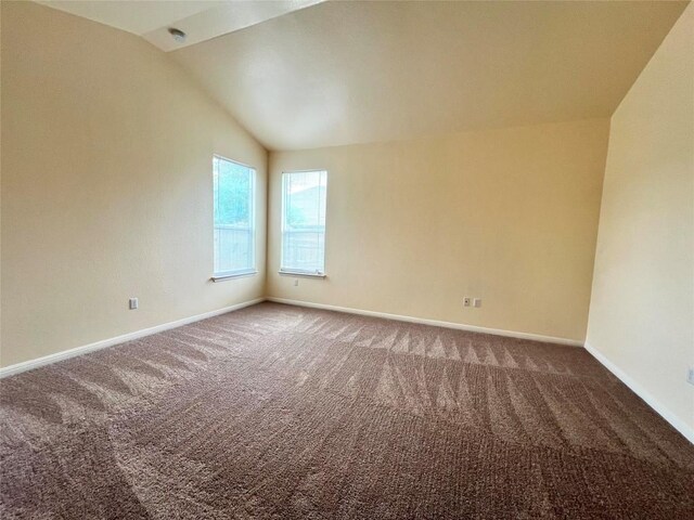 carpeted empty room featuring vaulted ceiling and baseboards