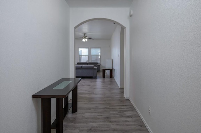 corridor featuring arched walkways, wood finished floors, and baseboards