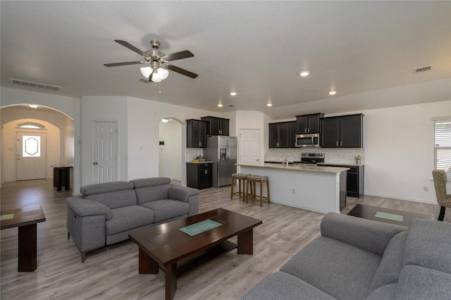 living area with visible vents, a ceiling fan, light wood finished floors, and arched walkways