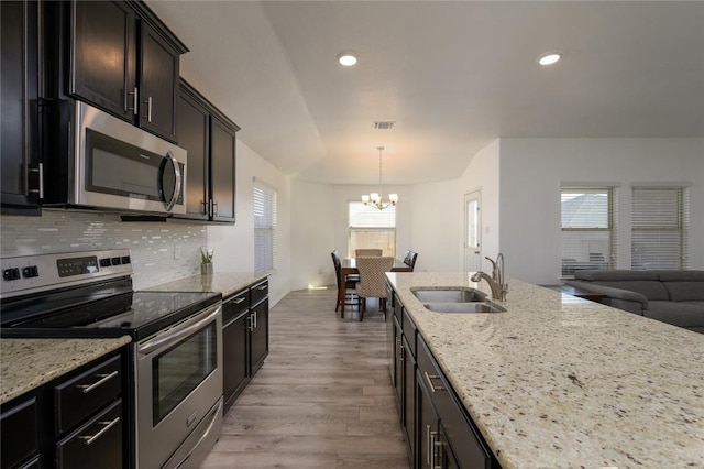 kitchen featuring a notable chandelier, a sink, light stone counters, and appliances with stainless steel finishes