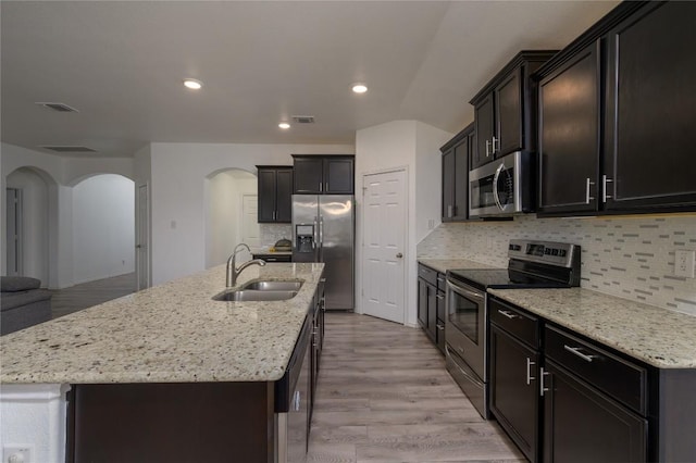 kitchen with a sink, visible vents, arched walkways, appliances with stainless steel finishes, and an island with sink