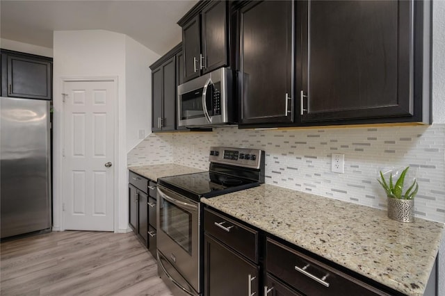 kitchen featuring tasteful backsplash, light stone countertops, light wood-style floors, and appliances with stainless steel finishes