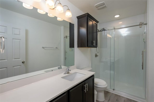 bathroom featuring wood finished floors, a shower stall, toilet, vanity, and visible vents