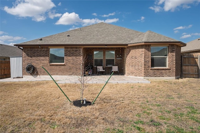 rear view of house with fence, roof with shingles, a patio, and brick siding