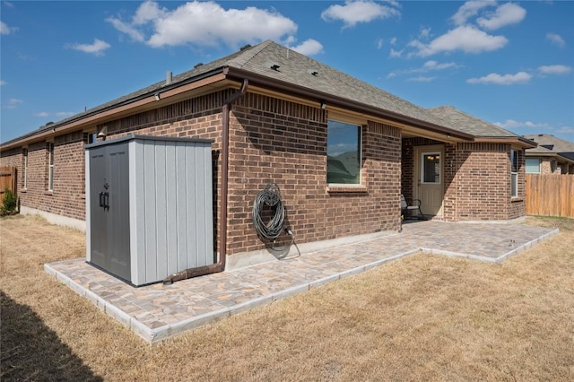 rear view of house featuring brick siding, fence, a shingled roof, and a patio area