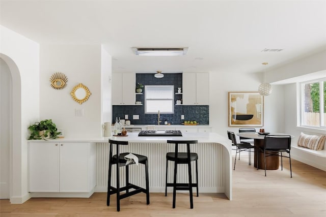 kitchen featuring decorative backsplash, a breakfast bar area, white cabinets, and arched walkways