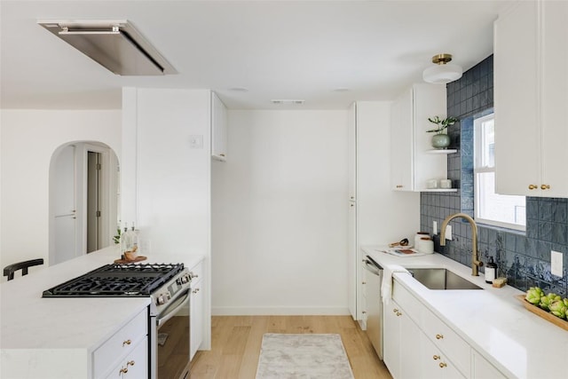 kitchen with open shelves, appliances with stainless steel finishes, a sink, arched walkways, and light wood-style flooring