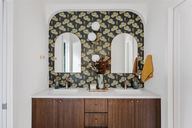 interior details with double vanity, wallpapered walls, a sink, and arched walkways