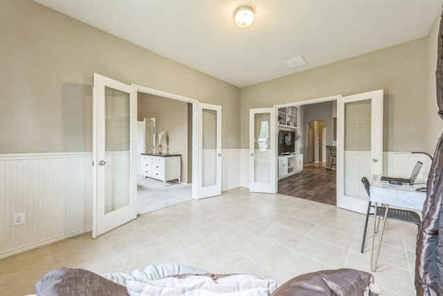 interior space featuring wainscoting, arched walkways, light tile patterned floors, and french doors