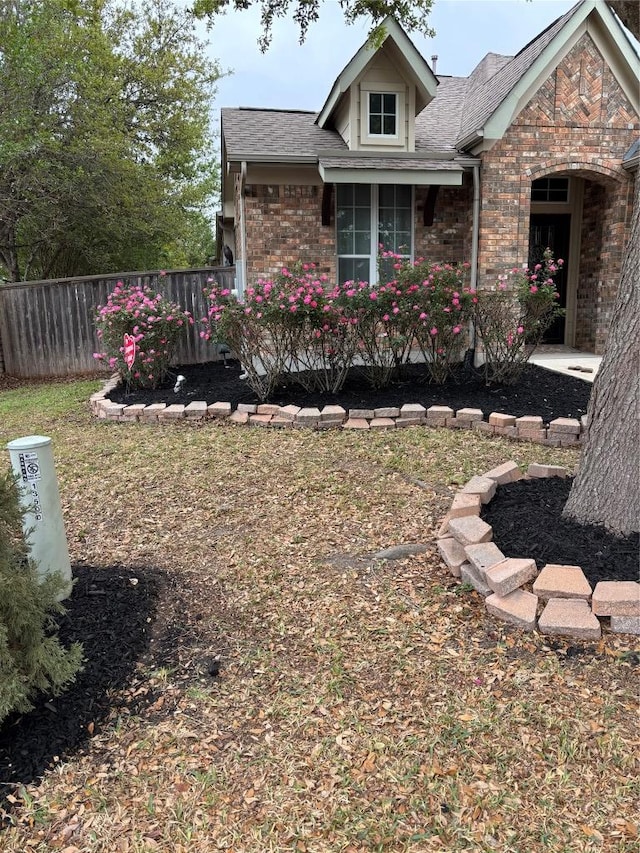 view of front of home featuring brick siding, fence, and a shingled roof