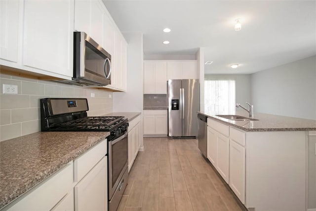 kitchen with appliances with stainless steel finishes, a sink, stone countertops, white cabinetry, and light wood-type flooring