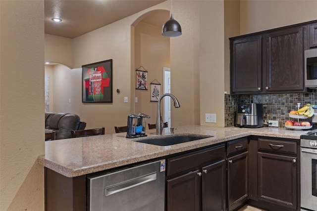 kitchen with a peninsula, dark brown cabinetry, arched walkways, a sink, and appliances with stainless steel finishes