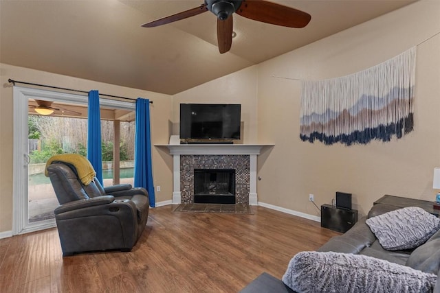 living area featuring a ceiling fan, vaulted ceiling, wood finished floors, a tile fireplace, and baseboards