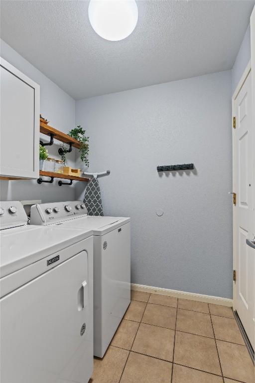 washroom with a textured ceiling, independent washer and dryer, cabinet space, light tile patterned floors, and baseboards