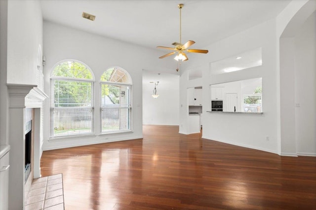 unfurnished living room with visible vents, a fireplace with flush hearth, wood finished floors, arched walkways, and a ceiling fan