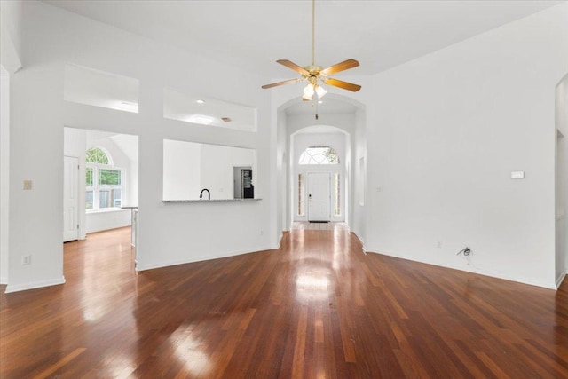 unfurnished living room with dark wood-style flooring, a ceiling fan, arched walkways, and a towering ceiling