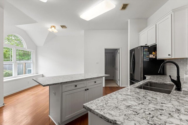 kitchen featuring a kitchen island, visible vents, light stone countertops, a sink, and freestanding refrigerator