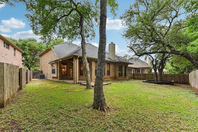 rear view of property featuring a lawn, a chimney, a fenced backyard, and a patio area