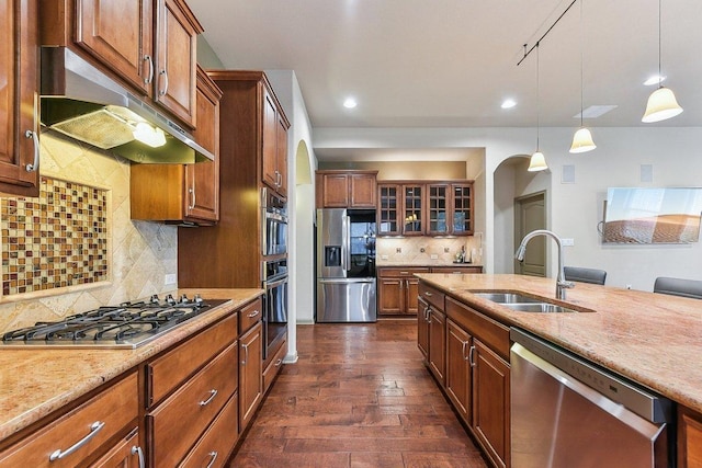 kitchen with under cabinet range hood, stainless steel appliances, arched walkways, and a sink