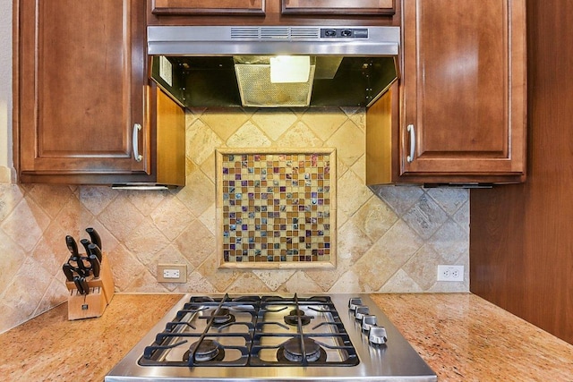 kitchen featuring stainless steel gas stovetop, light countertops, decorative backsplash, and under cabinet range hood