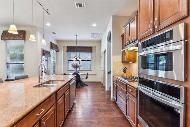 kitchen featuring dark wood-type flooring, brown cabinets, light stone counters, a sink, and appliances with stainless steel finishes