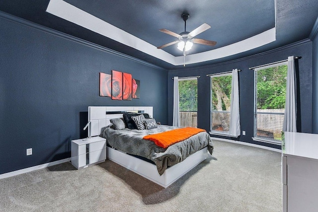 carpeted bedroom featuring crown molding, baseboards, a ceiling fan, and a tray ceiling