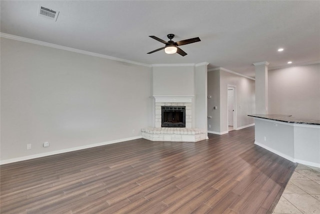unfurnished living room featuring a ceiling fan, visible vents, wood finished floors, baseboards, and ornamental molding