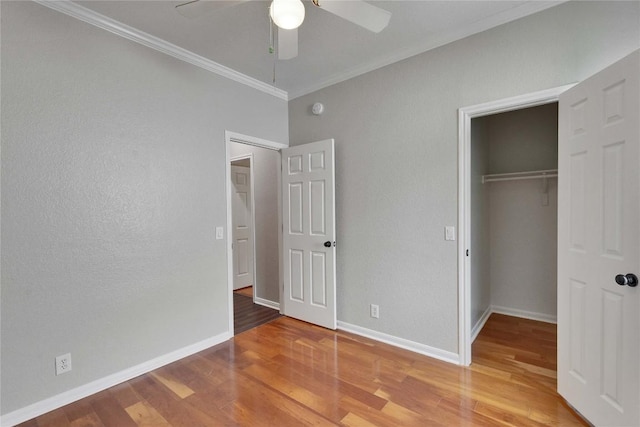 unfurnished bedroom featuring crown molding, a closet, wood finished floors, baseboards, and a ceiling fan