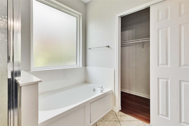 full bathroom featuring a garden tub, baseboards, and a walk in closet