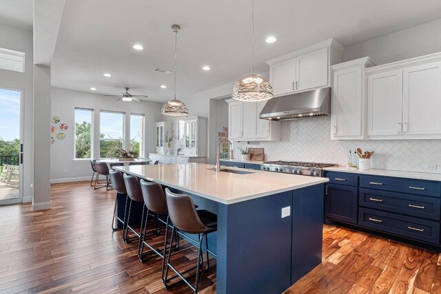 kitchen with a breakfast bar, a sink, light countertops, under cabinet range hood, and blue cabinets