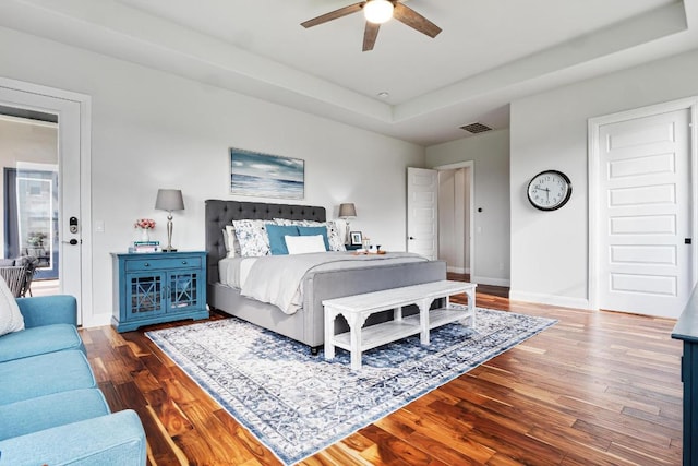 bedroom featuring visible vents, wood finished floors, baseboards, a tray ceiling, and a ceiling fan