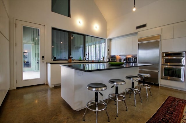 kitchen with stainless steel appliances, concrete flooring, white cabinetry, and a kitchen breakfast bar