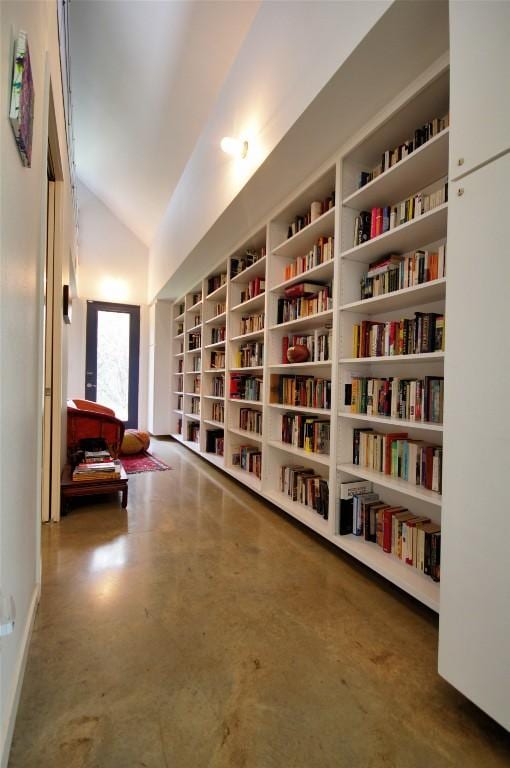living area with built in features, concrete flooring, bookshelves, and lofted ceiling