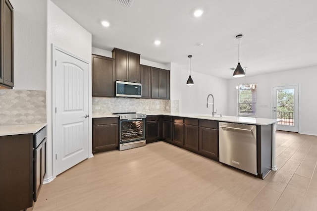 12126 Cantabria Rd, Austin, TX 78748 - kitchen featuring stainless steel appliances, a peninsula, light wood finished floors, dark brown cabinets, and light countertops