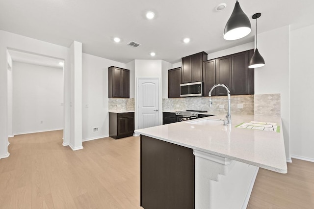 12126 Cantabria Rd, Austin, TX 78748 - kitchen featuring stainless steel appliances, light wood-type flooring, a peninsula, dark brown cabinetry, and tasteful backsplash