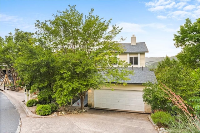 view of property hidden behind natural elements with an attached garage, roof with shingles, driveway, and a chimney