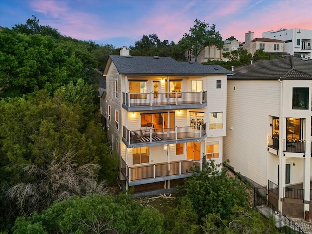 back of house at dusk with a chimney and a balcony