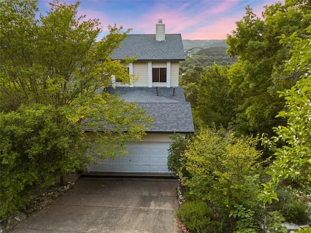 view of side of home with a garage, roof with shingles, driveway, and a chimney
