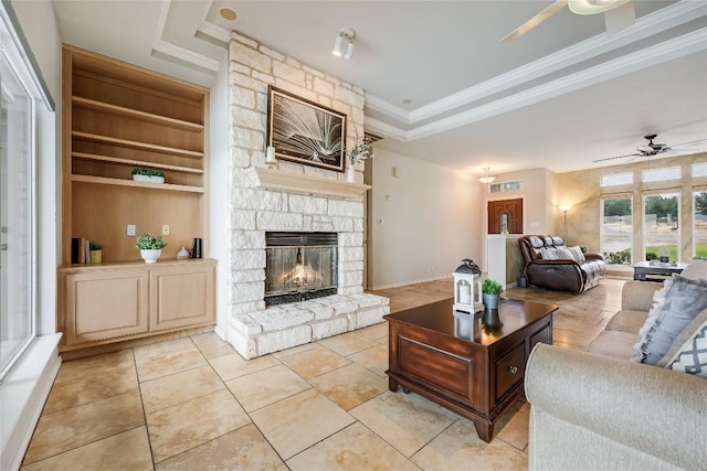 3606 Bunyan Cir, Lago Vista, TX 78645 - living room with a ceiling fan, a tray ceiling, a stone fireplace, crown molding, and light tile patterned flooring