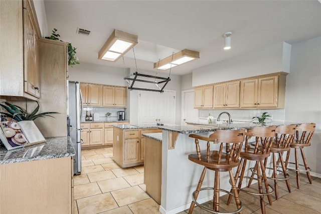 3606 Bunyan Cir, Lago Vista, TX 78645 - kitchen with light brown cabinets, a kitchen breakfast bar, tasteful backsplash, and stone countertops
