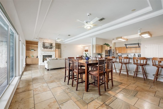 3606 Bunyan Cir, Lago Vista, TX 78645 - dining room featuring a raised ceiling, a ceiling fan, a stone fireplace, ornamental molding, and light tile patterned flooring